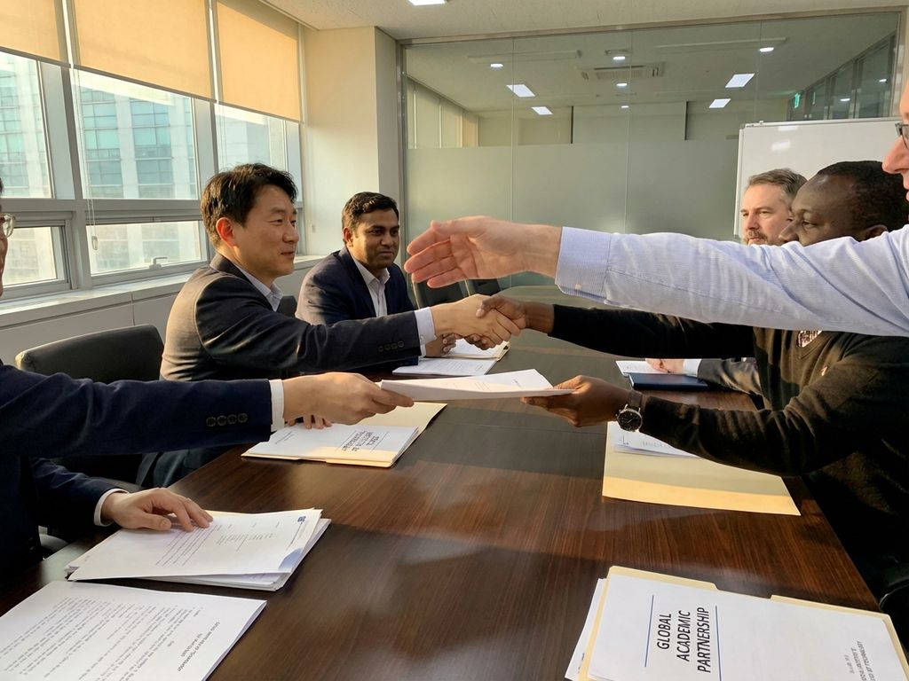 Diverse hands shaking across conference table with Asian research institute folders and international partnership documents